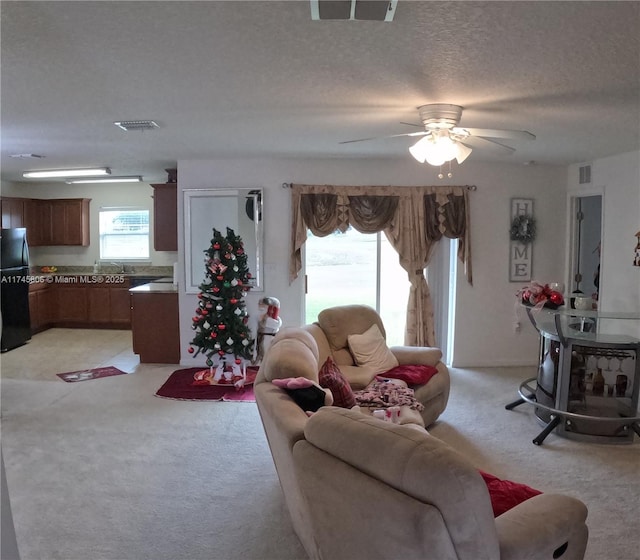 living area with visible vents, ceiling fan, and light colored carpet