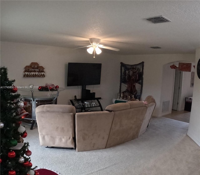 living area with carpet, visible vents, a ceiling fan, and arched walkways