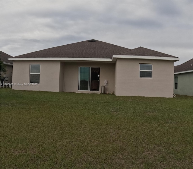 back of property with roof with shingles, stucco siding, and a lawn