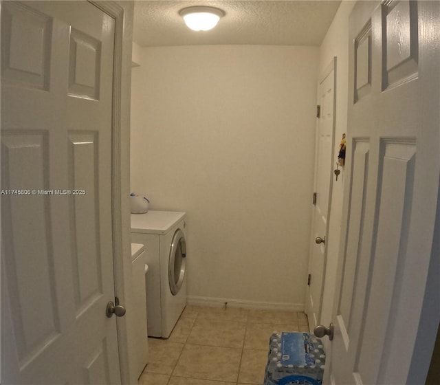clothes washing area featuring laundry area, a textured ceiling, light tile patterned floors, washing machine and dryer, and baseboards
