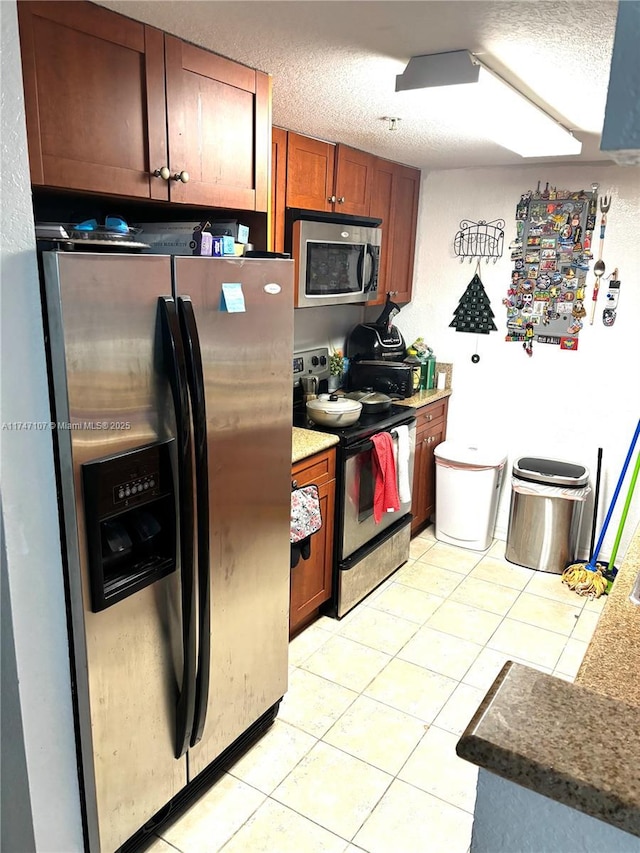 kitchen featuring stainless steel appliances, brown cabinets, light tile patterned flooring, and a textured ceiling