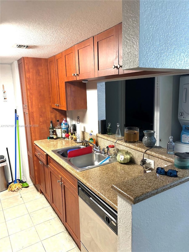 kitchen with brown cabinets, stacked washer / dryer, a sink, a textured ceiling, and dishwasher