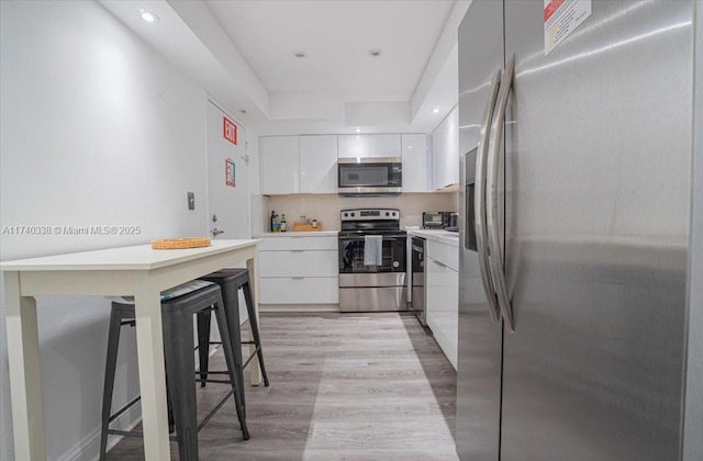 kitchen with appliances with stainless steel finishes, white cabinetry, light hardwood / wood-style flooring, and a breakfast bar