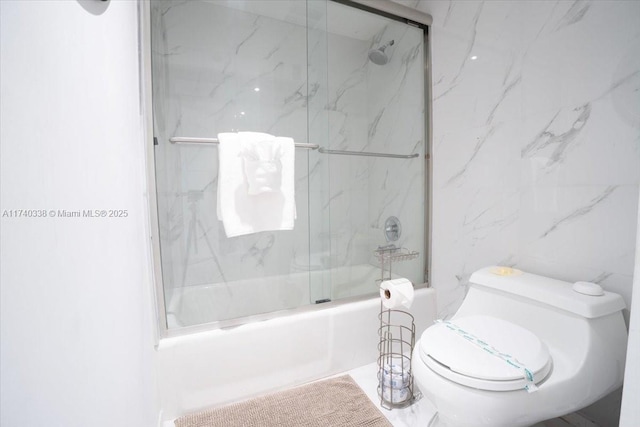 bathroom with toilet, tile walls, and combined bath / shower with glass door
