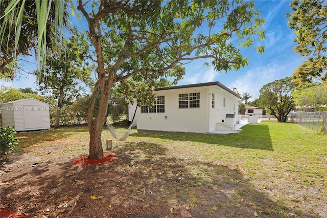 rear view of house with stucco siding, a lawn, a storage shed, fence, and an outdoor structure