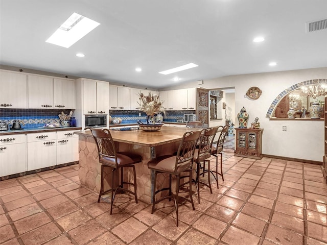 6200 SW 112th St, Pinecrest, FL 33156 - kitchen featuring decorative backsplash, stainless steel microwave, a skylight, a kitchen island, and a breakfast bar
