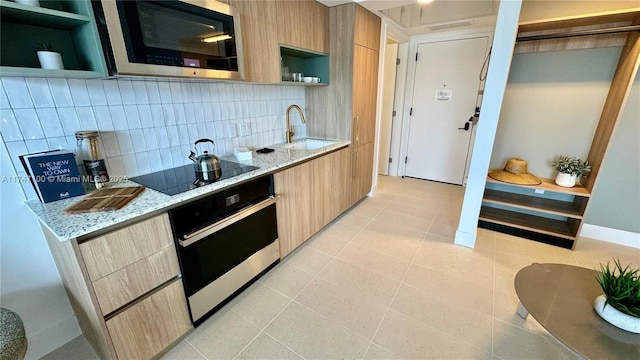 kitchen featuring black electric stovetop, light stone countertops, wall oven, light tile patterned flooring, and sink