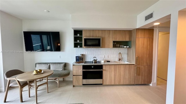 kitchen with light stone countertops, black appliances, decorative backsplash, light tile patterned floors, and sink