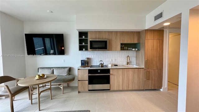 kitchen featuring light tile patterned floors, sink, backsplash, black appliances, and light stone countertops