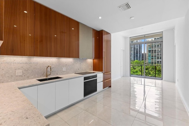 kitchen with tasteful backsplash, white cabinetry, black electric stovetop, sink, and oven