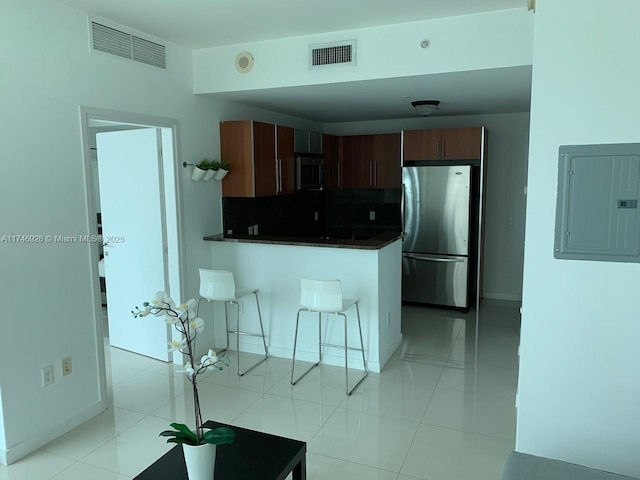 kitchen featuring electric panel, a breakfast bar, backsplash, light tile patterned floors, and stainless steel refrigerator