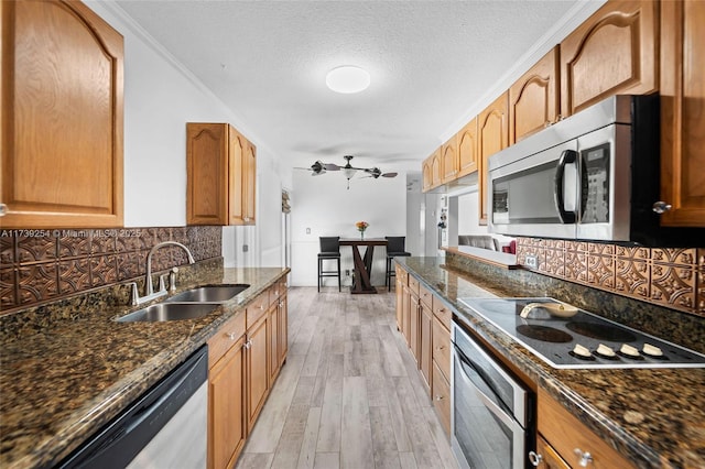 kitchen featuring light wood-style flooring, stainless steel appliances, dark stone counters, a sink, and backsplash
