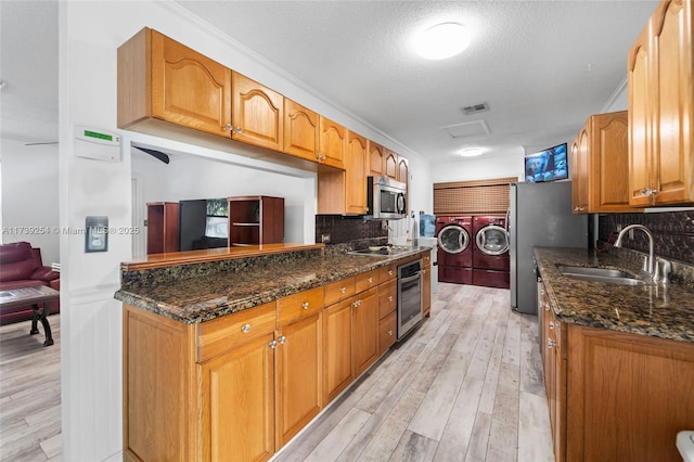 kitchen featuring stainless steel appliances, washer and dryer, backsplash, sink, and dark stone counters