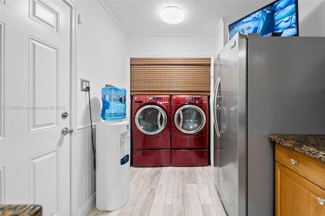 clothes washing area with ornamental molding, light hardwood / wood-style flooring, washing machine and clothes dryer, and a textured ceiling