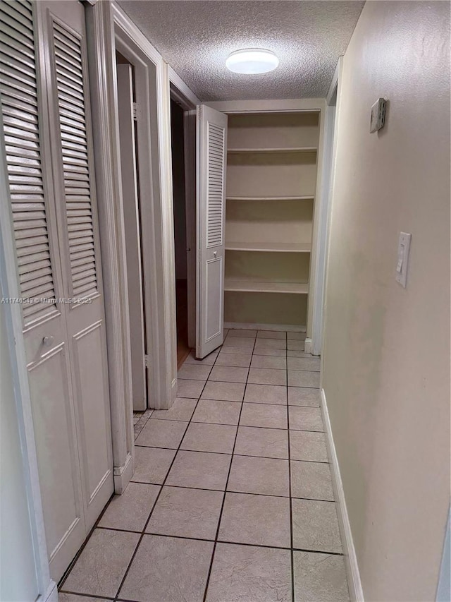 hall featuring a textured ceiling, light tile patterned floors, built in features, and baseboards