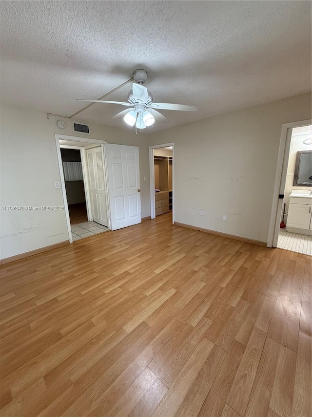 unfurnished bedroom featuring a textured ceiling, ensuite bath, visible vents, and light wood-style floors