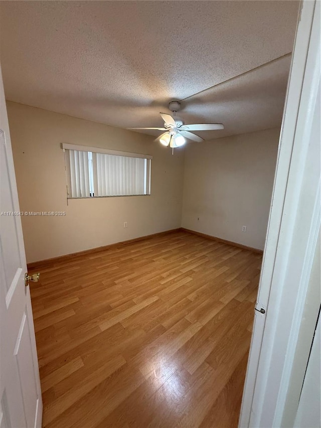 spare room featuring a ceiling fan, baseboards, a textured ceiling, and light wood finished floors