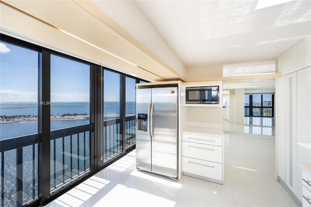 kitchen with light tile patterned flooring, a water view, white cabinetry, and stainless steel appliances