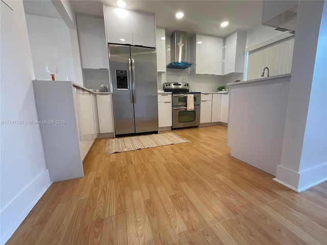 kitchen featuring appliances with stainless steel finishes, white cabinets, wall chimney range hood, and light hardwood / wood-style flooring