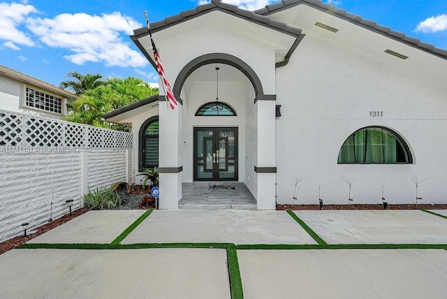 view of exterior entry featuring french doors, a tile roof, fence, and stucco siding