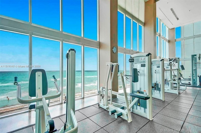 exercise room featuring a water view, expansive windows, and a towering ceiling