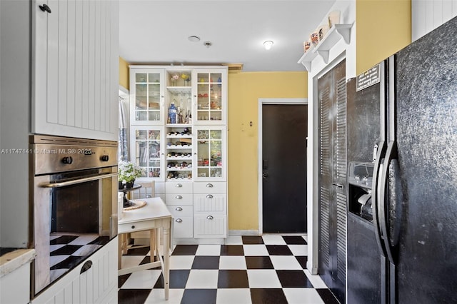 kitchen with white cabinets, oven, and black refrigerator with ice dispenser