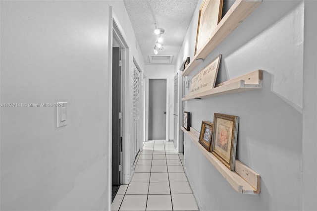 hallway with a textured ceiling, rail lighting, and light tile patterned flooring