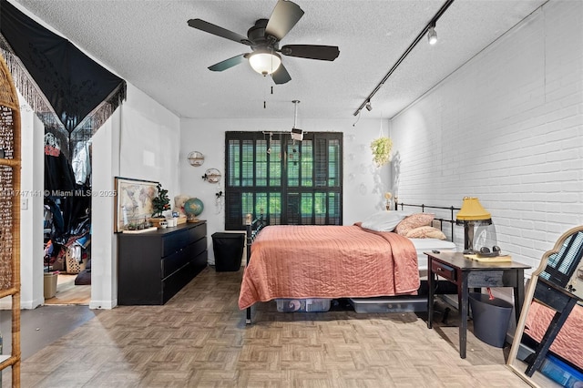 bedroom with rail lighting, a textured ceiling, ceiling fan, brick wall, and light parquet floors