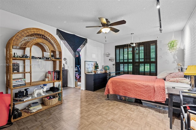 bedroom with ceiling fan, parquet flooring, track lighting, and a textured ceiling