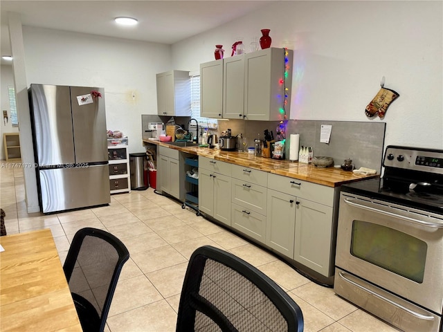 kitchen with appliances with stainless steel finishes, butcher block counters, light tile patterned floors, and tasteful backsplash