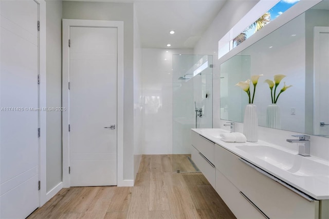 bathroom featuring double vanity, wood finished floors, walk in shower, and a sink