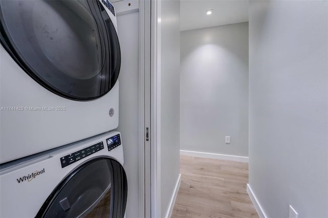 laundry area featuring light wood finished floors, laundry area, baseboards, and stacked washer and clothes dryer