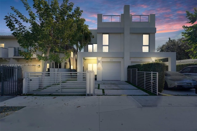 modern home featuring driveway, a fenced front yard, an attached garage, a gate, and stucco siding