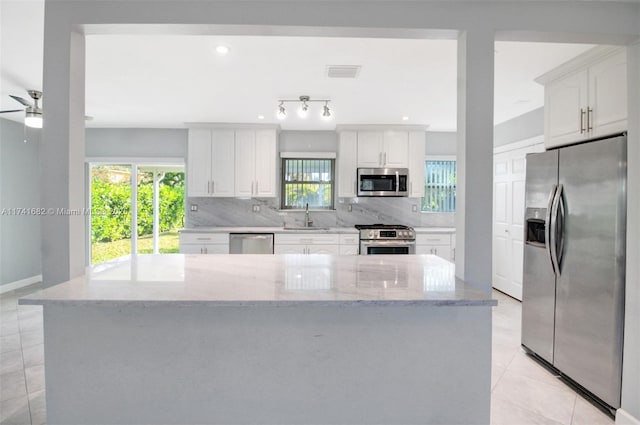 kitchen featuring stainless steel appliances, light stone countertops, decorative backsplash, sink, and white cabinetry