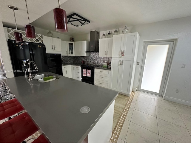 kitchen featuring hanging light fixtures, black appliances, wall chimney range hood, sink, and a kitchen bar