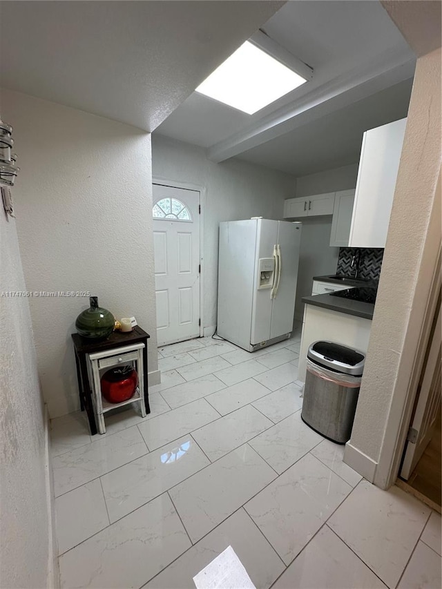 kitchen featuring white cabinets, white refrigerator with ice dispenser, and decorative backsplash