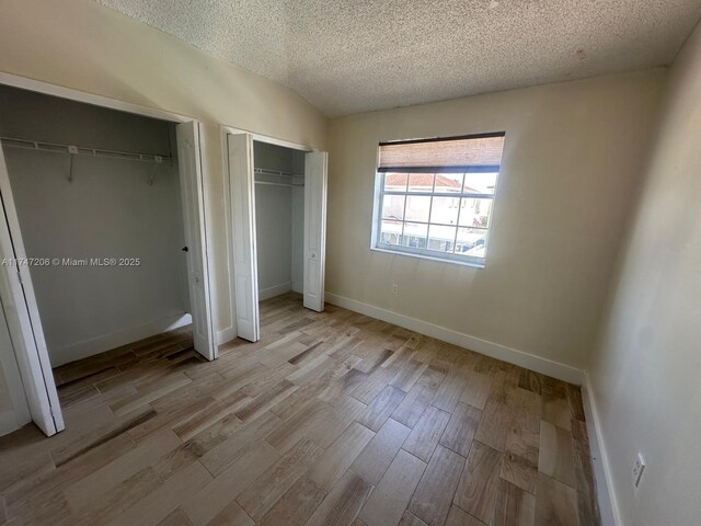 13926 SW 164th St, Miami, FL 33177 - unfurnished bedroom featuring multiple closets, a textured ceiling, light wood finished floors, and baseboards