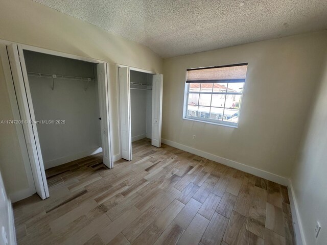 13926 SW 164th St, Miami, FL 33177 - unfurnished bedroom featuring multiple closets, a textured ceiling, light wood-style flooring, and baseboards