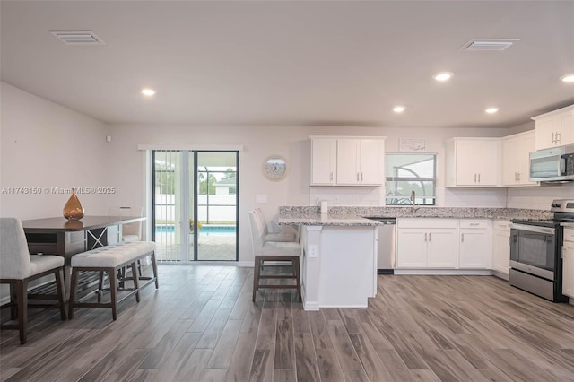 kitchen featuring stainless steel appliances, wood finished floors, visible vents, and white cabinetry