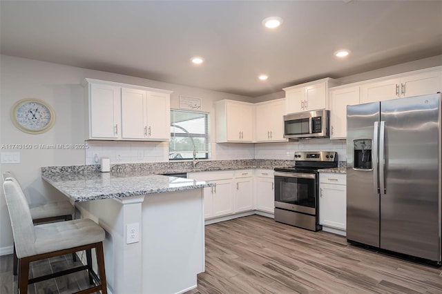 kitchen with a breakfast bar area, stainless steel appliances, backsplash, white cabinets, and a peninsula