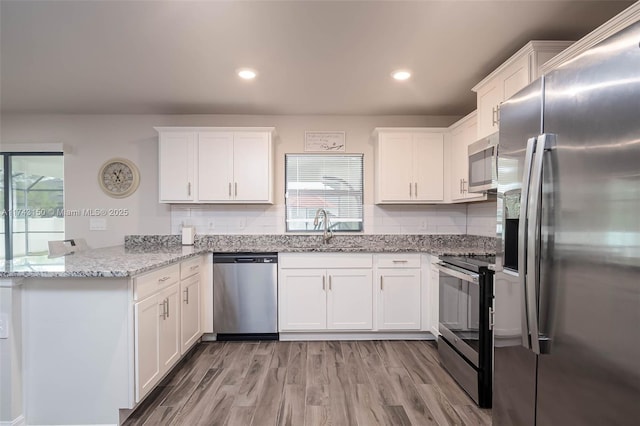 kitchen with stainless steel appliances, a peninsula, a sink, and white cabinetry