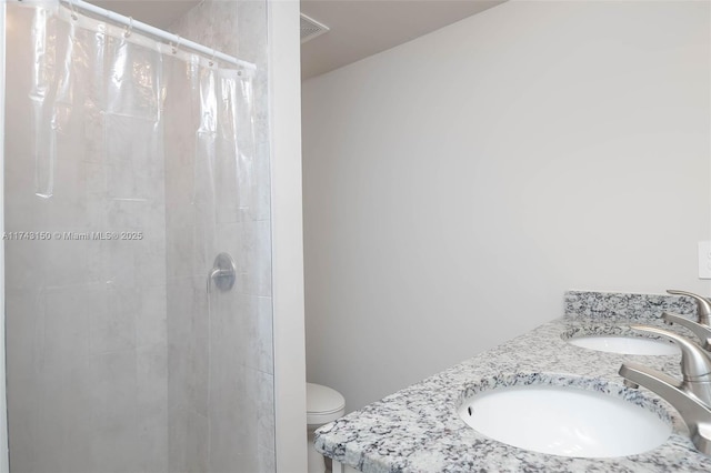 bathroom featuring a tile shower, double vanity, a sink, and toilet