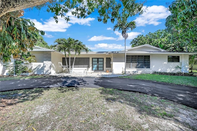 single story home with stone siding, stucco siding, driveway, and a front yard