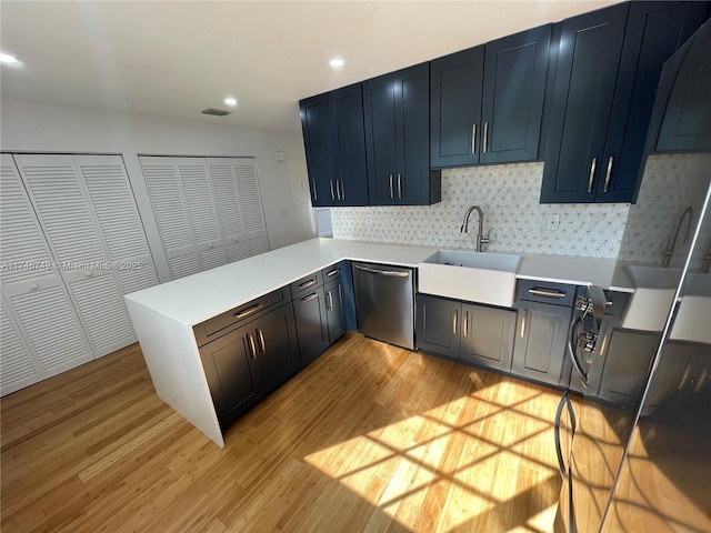 kitchen featuring kitchen peninsula, light hardwood / wood-style flooring, sink, backsplash, and stainless steel dishwasher