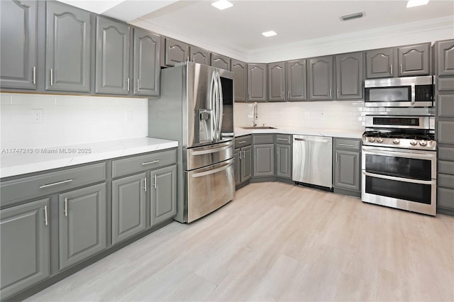 kitchen featuring gray cabinetry, stainless steel appliances, a sink, light countertops, and light wood finished floors