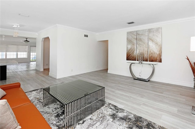 living area with arched walkways, light wood finished floors, visible vents, ornamental molding, and baseboards