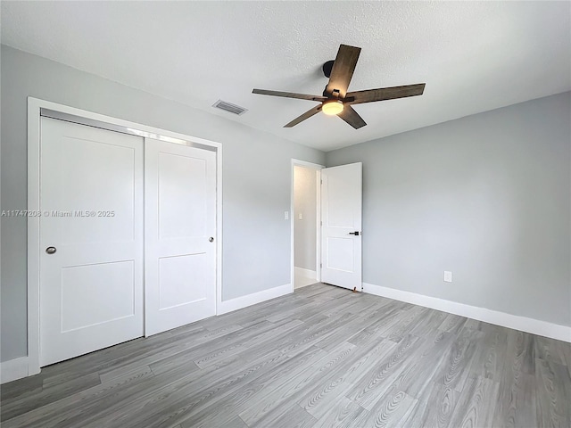 unfurnished bedroom featuring baseboards, a closet, visible vents, and wood finished floors