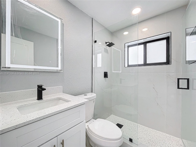 bathroom with a marble finish shower, recessed lighting, a textured wall, toilet, and vanity