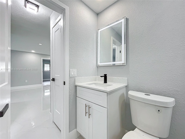 bathroom featuring marble finish floor, a textured wall, vanity, and toilet