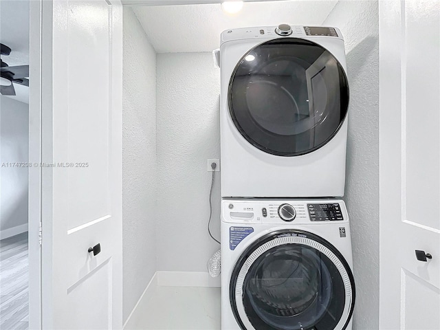 laundry area featuring a textured wall, stacked washer and dryer, laundry area, and baseboards